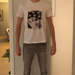 Vit t-shirt med pokertryck från Gildan - Säljer en vit t-shirt från Gildan med coolt pokertryck på bröstet, där man ser spelkort och marker i svart och grått. T-shirten har rund hals och korta ärmar, perfekt för dig som gillar unika prints och streetstyle.