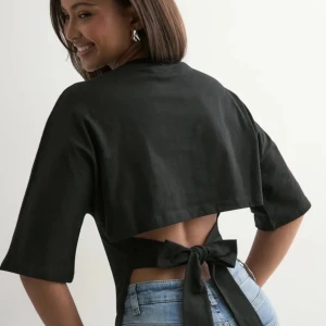 Svart bolerotopp med rosett från Nelly - Svart bolerotopp från Nelly med halvlånga ärmar och snygg öppen rygg som knyts med en stor rosett baktill. Toppens croppade passform gör den perfekt till jeans eller kjol. Materialet känns mjukt och har en lätt stretch.