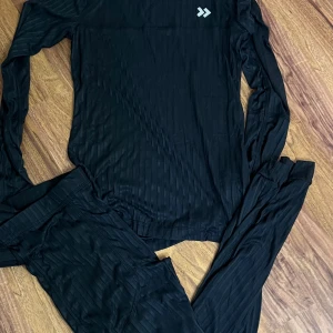 Svart långärmad träningströja 157 Funktion - Svart långärmad träningströja från 157 Funktion med diskreta ränder i materialet. Tröjan är tillverkad i lätt och snabbtorkande syntetmaterial, perfekt för löpning eller annan träning. Rund halsringning och logga på bröstet. Levereras med praktisk meshpåse.