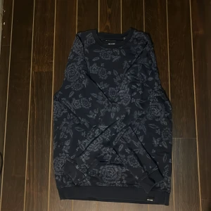 Blommig mörkblå tröja Only & Sons - Säljer en mörkblå sweatshirt från Only & Sons med snyggt blommigt mönster över hela tröjan. Klassisk rund halsringning och långa ärmar. Perfekt för dig som vill ha en stilren men ändå unik look.