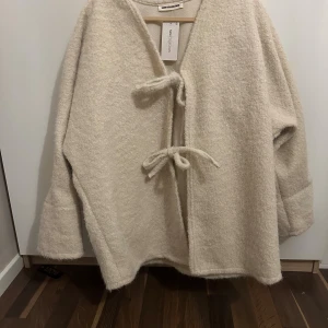 Beige omlottjacka med knyt - Mysig beige omlottjacka från New Collection med knyt framtill. Jackan har en loose passform, v-ringning och långa ärmar. Perfekt för lager-på-lager och en chill stil.