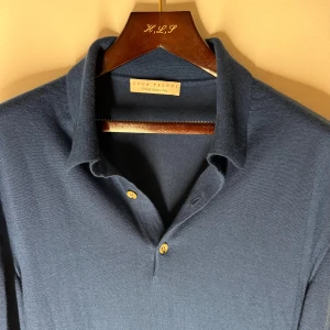 Luca Faloni polo - Snygg marinblå stickad polotröja från Luca Faloni i lyxig blandning av silke och kashmir. Tröjan har klassisk krage, tre knappar framtill och långa ärmar. Perfekt för dig som gillar stilrena och exklusiva plagg med mjuk känsla.