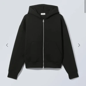 Svart hoodie med dragkedja Weekday - Svart hoodie från Weekday i storlek M. Tröjan har hel dragkedja framtill, huva och en stor ficka på magen. Modellen är loose fit med långa ärmar och ribbade muddar. Perfekt för chill dagar och enkel att matcha med jeans eller joggers.