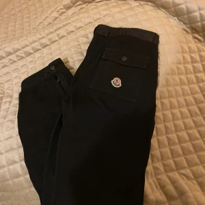 Svarta cargopants från Moncler - Säljer ett par svarta cargopants från Moncler. De är i storlek 164 barn men passar xs. Innerbenslängd: 70 cm. Midjemått: 36 cm