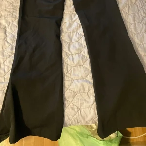 Svarta bootcut-byxor från Amisu - Svarta bootcut-byxor från Amisu i storlek 32. Byxorna har en klassisk, vid siluett med slits vid benslutet och är tillverkade i ett mjukt syntetmaterial. 