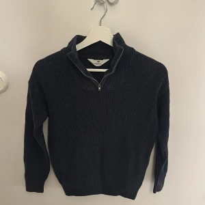 Mörkblå stickad half zip-tröja H&M - Mörkblå stickad tröja från H&M med ribbad struktur och half zip-dragkedja i halsen. Tröjan har långärmad passform och en hög krage som ger en chill och snygg look. Perfekt för dig som gillar enkel stil med lite edge.