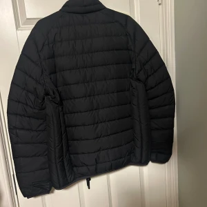 Svart pufferjacka från Parajumpers M - parajampers rescue squadron - Svart pufferjacka från Parajumpers i storlek medium. Jackan har broderad patch på ärmen, quiltad design och klassisk pufferlook. Slim fit-modell med snygga detaljer och sportig känsla. Perfekt för dig som vill ha en stilren och varm jacka med streetvibe.