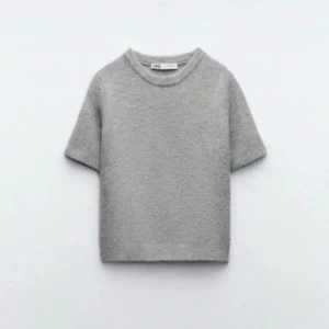 Grå stickad kortärmad tröja från Zara - Supermjuk grå stickad tröja från Zara med korta ärmar och rund hals. Tröjan har en enkel och clean look med ribbade kanter vid ärmslut och nederkant. Perfekt att styla med jeans eller kjol för en chill vibe. Kan gå ner i pris