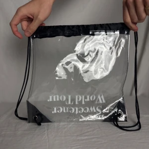 Sweetener World Tour genomskinlig ryggsäck - Genomskinlig väska med svart snörning och detaljer, tryck med texten 'Sweetener World Tour' på framsidan. Fick i VIP paket under Ariana Grandes spelning i Stockholm 2019 🌸