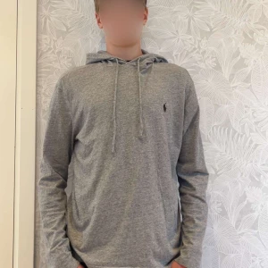 Grå hoodie från Ralph Lauren - Säljer en stilren grå hoodie från Ralph Lauren med klassisk huva och snörning. Skick 10/10. Modellen är 175 cm lång.