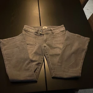 Gråa jeansbyxor från 157 Paris Patch - Snygga grå jeansbyxor från 157 Paris Patch med bootcut och klassiska fickor både fram och bak. Byxorna har dubbla knappar i midjan och är tillverkade i ett mjukt bomullsmaterial. Perfekta för dig som gillar en clean och enkel stil. Det är ett litet hål under gylfen, därav priset. 