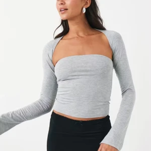 Grå croppad bolerotopp - Snygg grå croppad bolerotopp med lång ärm och axelbandslös design. Toppen har en tight passform och är tillverkad i mjukt bomullsmaterial som sitter skönt mot kroppen. Perfekt för dig som gillar trendiga och minimalistiska plagg.