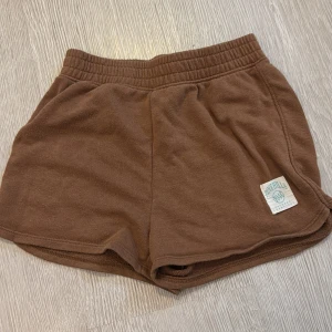 Bruna mjuka shorts från H&M - Säljer ett par bruna shorts från H&M med elastisk midja och mjukt bomullsmaterial. De har en avslappnad passform och en liten Pine Hills 94 patch framtill. Perfekta för chill dagar.