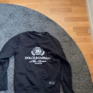 Svart Dolce & Gabbana sweatshirt - Svart sweatshirt från Dolce & Gabbana med vit logga och text framtill. Tröjan har rund halsringning och långa ärmar. Tillverkad i mjukt bomullsmaterial, perfekt för en chill och stilren look.