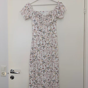 Blommig långklänning från Cider - Supersöt helt ny långklänning från Cider med blommigt mönster i pastellfärger. Klänningen har puffiga korta ärmar och snörning framtill. Perfekt för sommarens alla tillfällen. Lätt och luftig känsla. 
