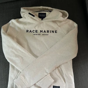 Beige hoodie från Race Marine - Säljer en beige hoodie från Race Marine med svart tryck framtill. Tröjan har huva, känguruficka och långa ärmar. Säljer pga att den inte har kommit till användning. Hoodien är i storlek S men jag skulle säga att passformen lutar mer åt xs.