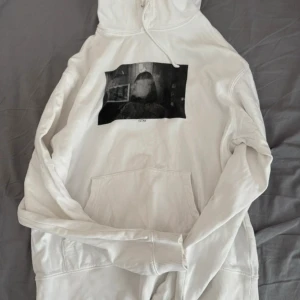 Vit hoodie från STAY med tryck - Säljer en vit hoodie från STAY i storlek M. Tröjan har ett svartvitt tryck framtill med motiv och texten 'STAY' under. Klassisk känguruficka, huva med snörning och mjukt material. Perfekt för dig som gillar streetwear och enkel stil🩷