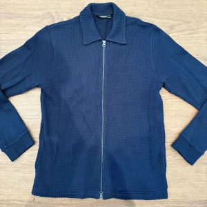 Marinblå cardigan J.Lindeberg - Säljer en marinblå cardigan från J.Lindeberg med hel dragkedja framtill och klassisk krage. Den är i nyskick och aldrig använd! Storlek S.