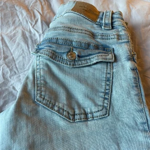 Ljusblå bootcut jeans med ficklock - Snygga ljusblå jeans från Perfect Jeans med bootcut passform. Jeansen har klassiska fickor med lock och knapp bak, bälteshällor och dragkedja fram. Perfekta för dig som gillar en retroinspirerad look och vill ha ett par jeans som sticker ut.
