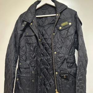 Svart quiltad jacka från Barbour - Snygg svart quiltad jacka från Barbour med guldiga detaljer. Strl 34