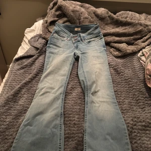 Bootcut jeans i ljusblå denim från Nelly - Bootcut jeans från Nelly i ljusblå tvättad denim med klassiska fem fickor och dubbla silverfärgade knappar framtill. Snygga kontrastsömmar i orange och normal passform. Perfekta för dig som gillar retrovibbar och vill ha ett par jeans med lite extra attityd.