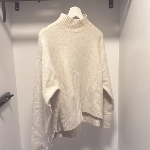 Beige polotröja med ribbade detaljer - Mysig beige polotröja med hög krage och ribbade muddar vid ärmslut och nederkant. Tröjan har en loose passform och är perfekt för kyliga dagar. Enkel att matcha med jeans eller kjol för en chill look.