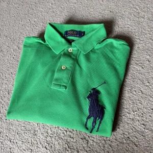 Grön pikétröja Polo Ralph Lauren S - Snygg grön pikétröja från Polo Ralph Lauren i slim fit-modell. Tröjan har klassisk krage, knäppning med två knappar, stor marinblå broderad logga på bröstet och en stor siffra 3 på ärmen. Perfekt för dig som gillar sportig och stilren look.