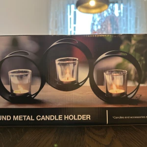 Round Metal Candle Holder - Elegant rund metall-ljushållare med plats för tre värmeljus i glas. Modern design som passar både vardagsrum och matsal. Produkten ser ut att vara i nyskick utan synligt slitage eller defekter. Perfekt för att skapa mysig stämning hemma.