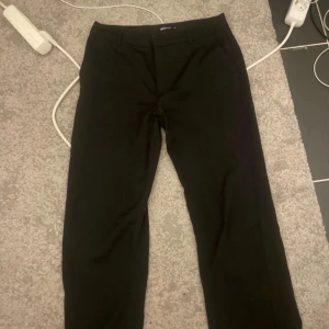 Svarta kostymbyxor Gina Tricot  - Svarta kostymbyxor från Gina Tricot i storlek 38. Klassisk rak modell med hällor för bälte och diskreta bakfickor. Perfekta för en clean och stilren look. Materialet känns mjukt och följsamt.