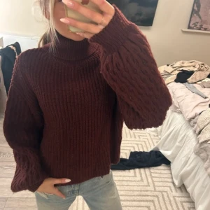 Vinröd polotröja med kabelstickade ärmar - Säljer en vinröd polotröja med grovstickade kabelmönstrade ärmar och hög krage. Tröjan har en loose passform och är stickad i ett mjukt material som känns riktigt cozy. Perfekt för kyliga dagar och snygg till jeans.