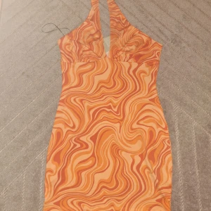 Orange swirl kortklänning H&M M - Säljer en kort klänning från H&M i storlek M med ett snyggt swirlmönster i olika orange toner. Klänningen har halterneck och figurnära passform, perfekt för dig som gillar färg och vill sticka ut. Materialet är mjukt och stretchigt för en bekväm känsla.