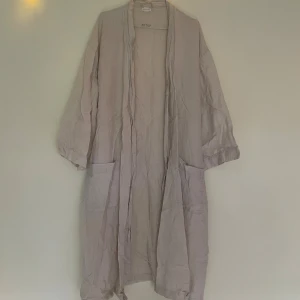 Beige morgonrock i linne från H&M - Morgonrock från H&M i 100% linne. Modellen är rak med stora fickor framtill.