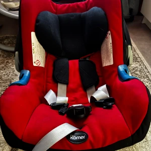 Römer Babyskydd - Römer babyskydd i rött och svart. Sätet är i gott skick med mindre ytliga repor på plasten, men inga synliga skador på tyget bara på ettiketen. Passar för säker transport av spädbarn i bil. Enkel installation och tydliga instruktioner på sidan.