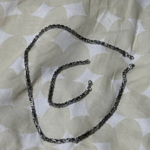 Kedjehalsband (60) och armband (21cm)i silverfärg - Säljer ett set med ett halsband och ett matchande armband i silverfärg. Båda har en robust kedjedesign med rejäla länkar och karbinlås. Perfekt för dig som gillar en stilren och edgy look.