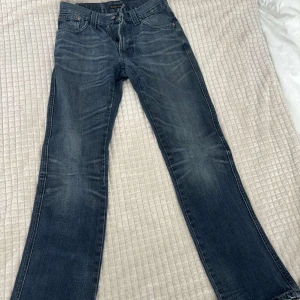 Blå bootcut jeans från Nudie Jeans - Snygga blå jeans från Nudie Jeans med klassisk bootcut-passform. Jeansen har slitna detaljer, fem fickor och läderpatch med logga bak. Tillverkade i robust denim med tydliga kontrastsömmar och dragkedja framtill.