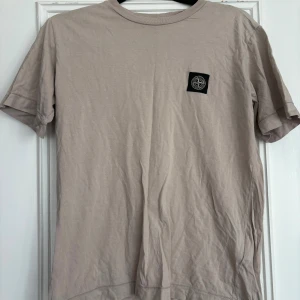 Beige t-shirt från Stone Island Junior - Snygg beige t-shirt från Stone Island Junior med klassisk logopatch på bröstet. T-shirten har rund halsringning och korta ärmar. Tillverkad i mjuk bomull för en skön känsla och clean look.