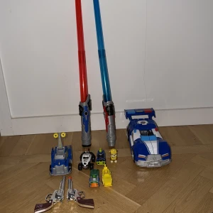 Diverse leksaker säljes  - Bilden visar en samling leksaker, inklusive två ljussablar, leksaksbilar, robotar och två leksakspistoler. Produkterna är färgglada och ser ut att vara i gott skick, men det finns inga synliga elektronikprodukter eller kända märken/modeller relaterade till elektronik.