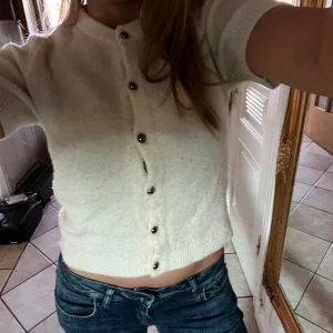 Vit stickad kortärmad topp Gina Tricot - Superfin vit stickad topp från Gina Tricot med korta ärmar och rund hals. Toppen har snygga silvriga knappar framtill och ribbade kanter vid ärmslut och nederkant. Perfekt till jeans eller kjol för en clean look.