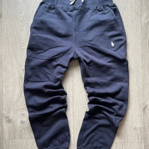 Mörkblå mjukisbyxor Polo Ralph Lauren - Mörkblå mjukisbyxor från Polo Ralph Lauren med vit broderad logga på höften. Byxorna har resår och snörning i midjan samt muddar vid bensluten. Tillverkade i mjuk bomull för maximal komfort.