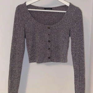 Grå ribbad croppad topp från SHEIN - Grå croppad topp från SHEIN med ribbad struktur och rund halsringning. Toppen har långa ärmar och knappar framtill som snygg detalj. Perfekt att styla med höga jeans eller kjol för en chill look.