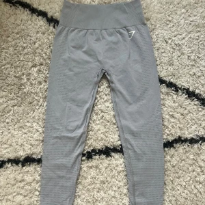 Gymshark Träningstights <3 - Snygga grå leggings från Gymshark med hög midja och diskret mönstrad struktur längs benen. Stretchigt material i polyester och elastan som sitter tight och bekvämt. Perfekta för träning och har en stilren logga framtill.