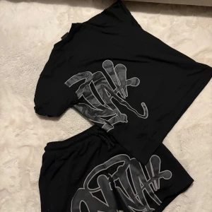 Syna world set i svart och grått - Svart t-shirt med stort grått syna logga med tryck på både fram- och baksidan. T-shirten har en klassisk rund hals och korta ärmar. Samt ett par likadana shorts med samma design. 