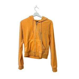 Juicy Couture orange mjukisset - Säljer ett ikoniskt oranget mjukisset från Juicy Couture med bootcut-snitt och snörning i midjan. Byxorna har stora fickor fram och är gjorda i mjuk velour som ger den perfekta Y2K-viben. Perfekt för dig som vill sticka ut och köra full Paris Hilton-stil. Använd fåtal ggr. Strlk S men passar även M  pga stretchig. 