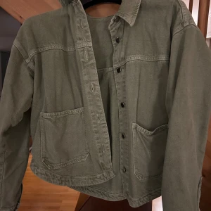 Grön jeansjacka  från Zara - Snygg grön overshirt från Zara med klassisk krage och två stora fickor framtill. Jackan har knappar hela vägen och är tillverkad i bomullsmaterial. Perfekt att slänga på över en t-shirt för en chill look.