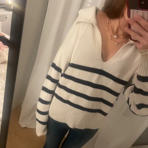 Randig stickad tröja från Gina Tricot - Superfin vit stickad tröja från Gina Tricot med mörkblå ränder. Tröjan har v-ringning, krage. Perfekt för en chill och snygg look, passar till jeans eller kjol.