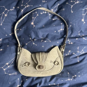 Grön axelväska i manchester - Snygg grön axelväska i mjukt manchestertyg med justerbar rem och coola metalldetaljer som jag fick i födelsedagspresent två år sedan och nu bara samlar damm i garderoben numera. Väskan har ett lock med vridknapp och ett rymligt fack med innerficka som stängs med dragkedja. Perfekt storlek för mobil, plånbok och småsaker.