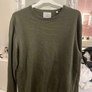 Olivgrön tröja från Bläck - En stilren olivgrön tröja från Bläck med rund halsringning och långa ärmar. Tröjan har en klassisk passform och är tillverkad i mjuk bomull, perfekt för lager-på-lager under höst och vår. Storlek L och väldigt fint skick! Nypris ligger runt 600kr
