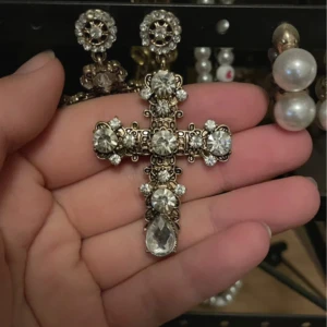 Korsörhängen  - Säljer ett par stora statement-örhängen i form av kors, dekorerade med gnistrande klara stenar och guldfärgad metall. Örhängena har en lyxig vibe med många detaljer och stora droppformade stenar längst ner. Perfekta för dig som vill sticka ut och älskar bling! Köpta från Urban Outfitters😇 Aldrig använda!