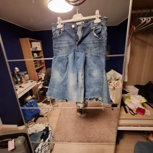 Blå jeanskjol från Lindex, strl 32 - Säljer en cool blå jeanskjol från Lindex med hög midja och rå kant nertill. Kjolen har fickor både fram och bak, samt knapp och dragkedja framtill. Materialet är klassisk denim och kjolen har en lätt utsvängd form som ger en avslappnad vibe. Skulle säga att kjolen passar 32-38. Den är handsydd.💞