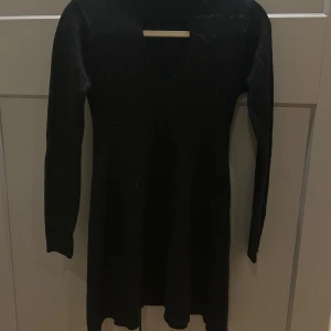 Svart stickad klänning från Ultra flirt - Svart stickad klänning med lång ärm och v-ringad hals från Ultra Flirt.  Modellen är kort och har en mjuk, stretchig känsla tack vare materialet. Perfekt för dig som gillar enkel och stilren design med lite edge.